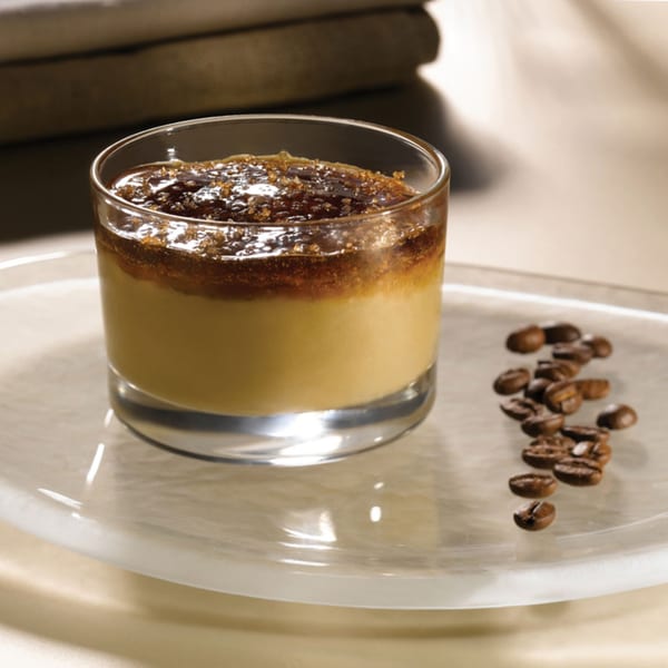 Coffee panna cotta dessert in a glass with coffee beans on a clear plate.