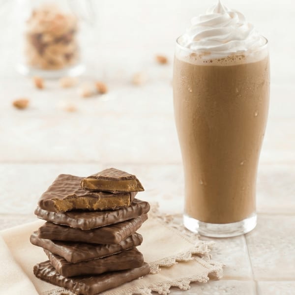 A tall glass of iced coffee with whipped cream next to a stack of chocolate toffee bars.
