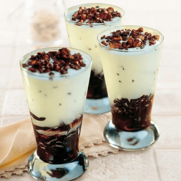 Three parfait glasses filled with layered vanilla cream, chocolate sauce, and chocolate crumbles.